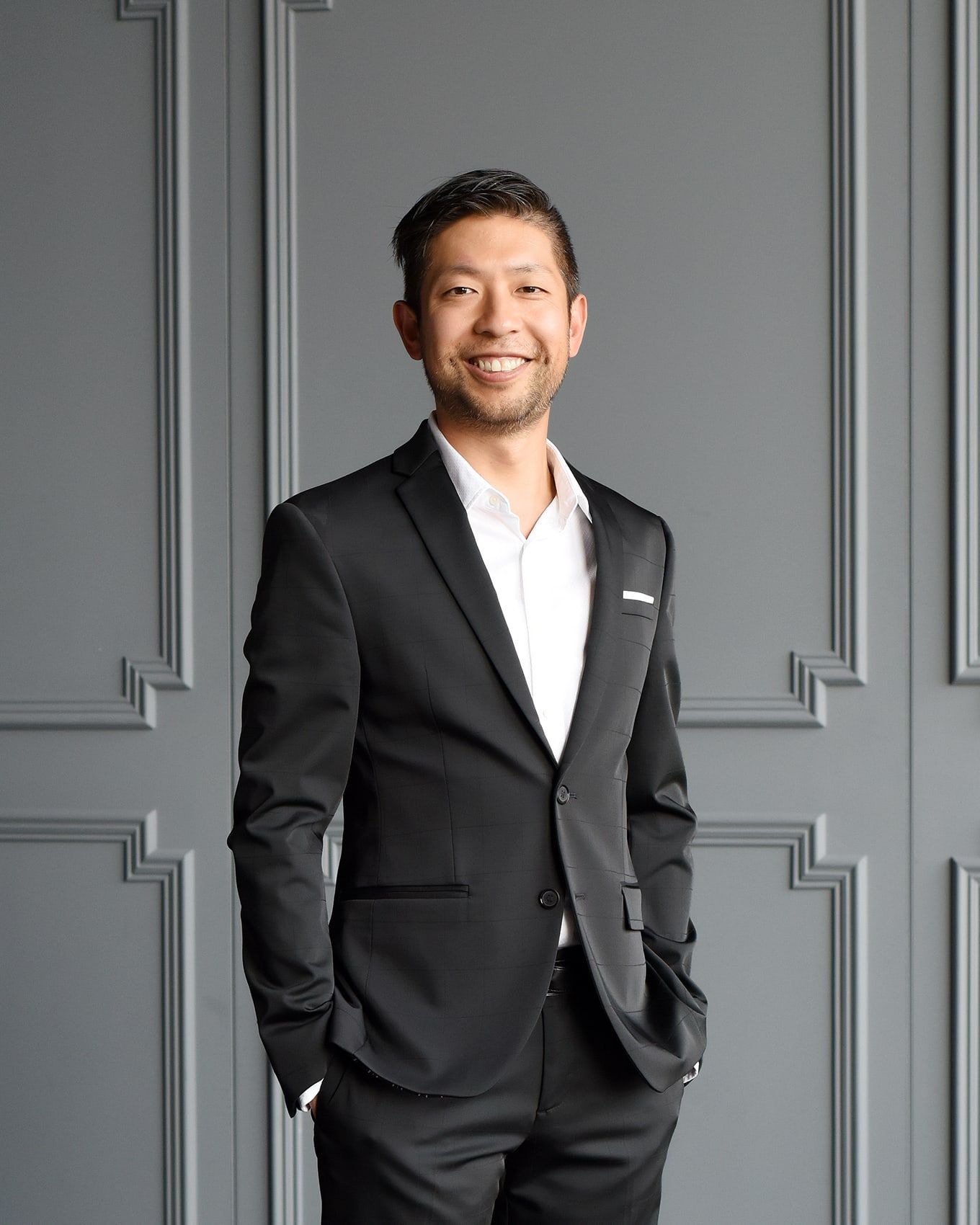 Kirby Chan, Broker, standing in a dark suit and smiling