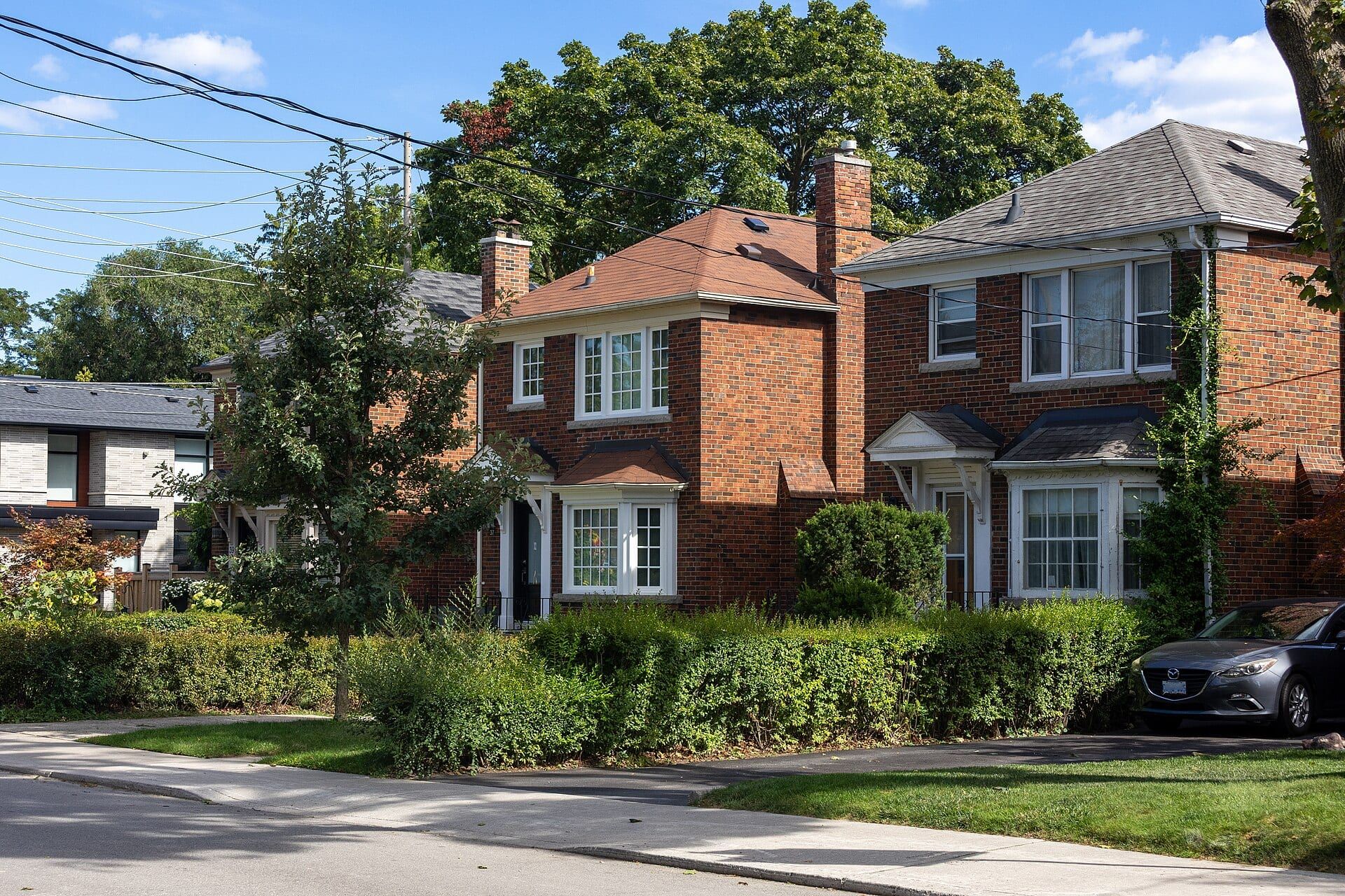 Brick houses behind green lawns and hedges along Rumsey Road in Leaside, Toronto.
