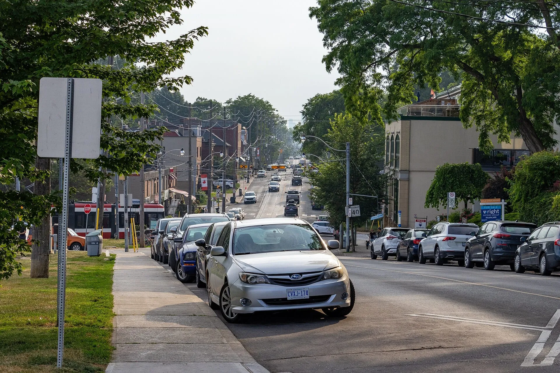 Shops and parked cars along a leafy stretch of Queen Street East in The Beaches, Toronto.